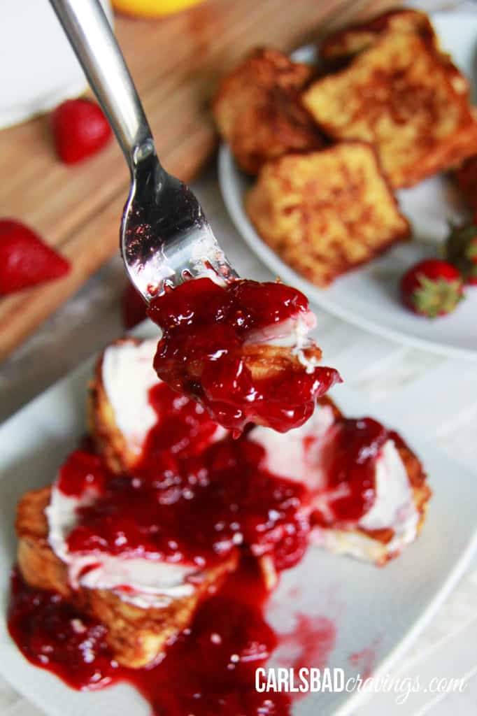 A fork with Angel Food Cake French Toast with strawberry syrup over top on a white plate.