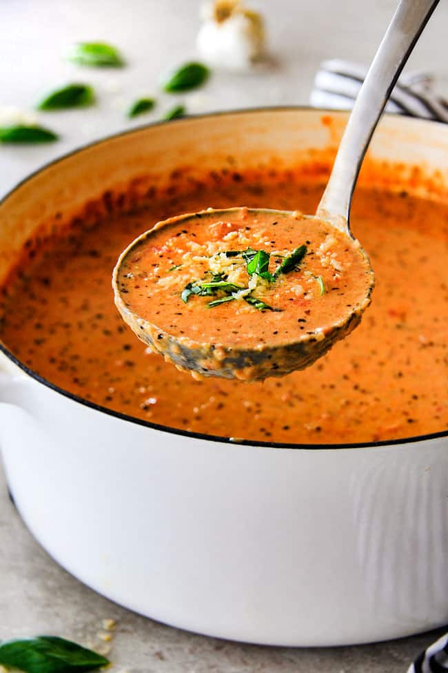 serving creamy tomato basil soup with a silver ladle.