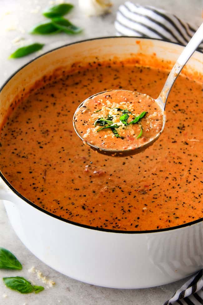 a ladle of Creamy Tomato Basil Soup raised above a big soup pot. 