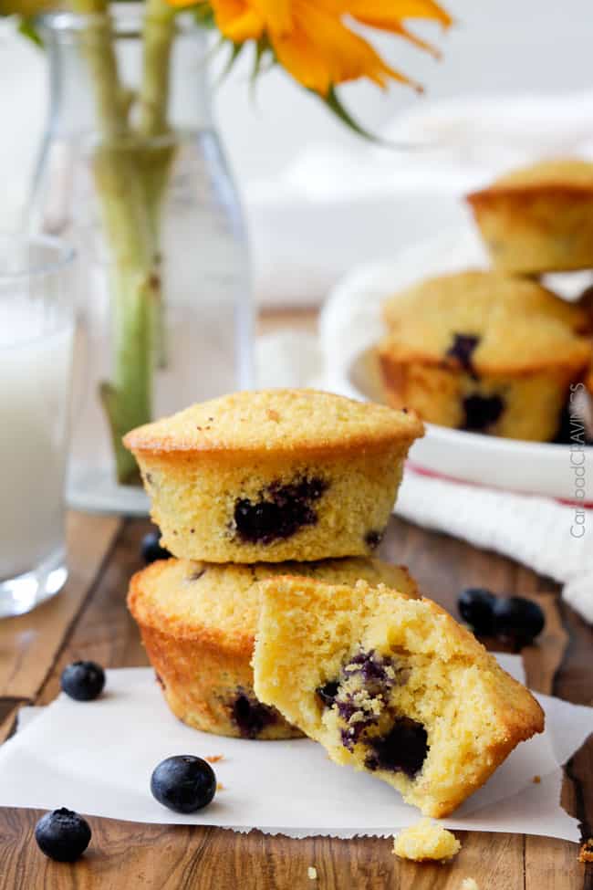 three blueberry cornmeal muffins. two are stacked, one sits in front with a bite missing. 