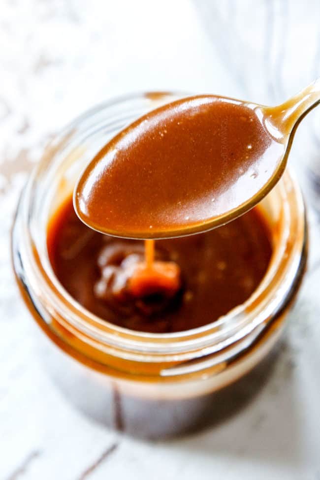 homemade caramel sauce drizzling from a spoon into a jar of caramel