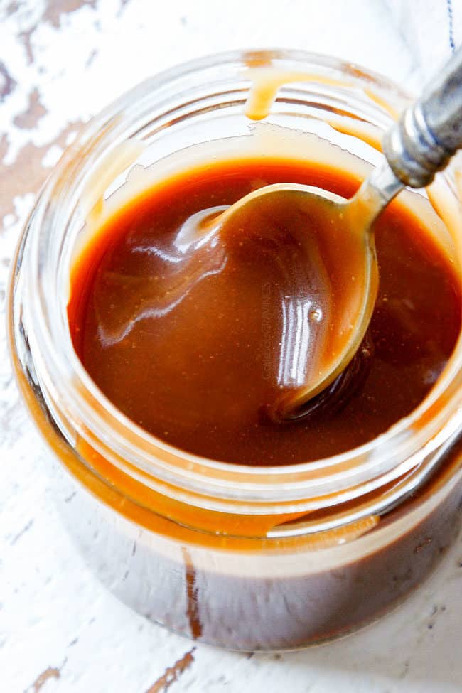side view of a spoon dipping into a jar of best caramel sauce