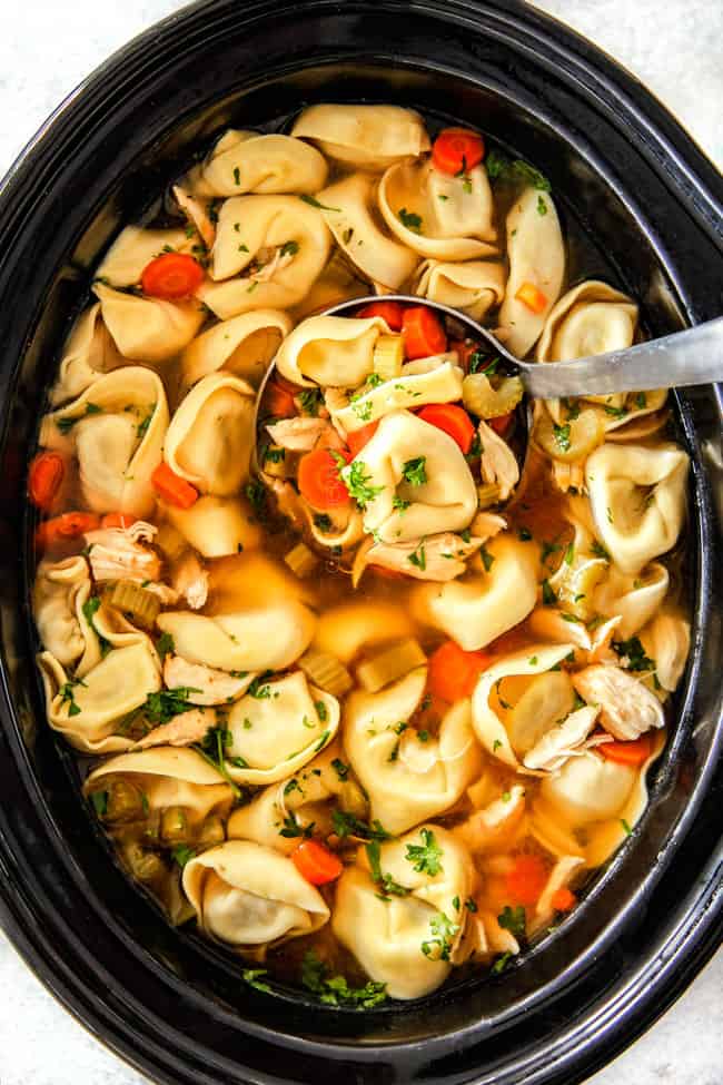 Chicken Tortellini Soup with cheese tortellini, carrots, celery, onions, garlic and spices in crockpot with soup ladle