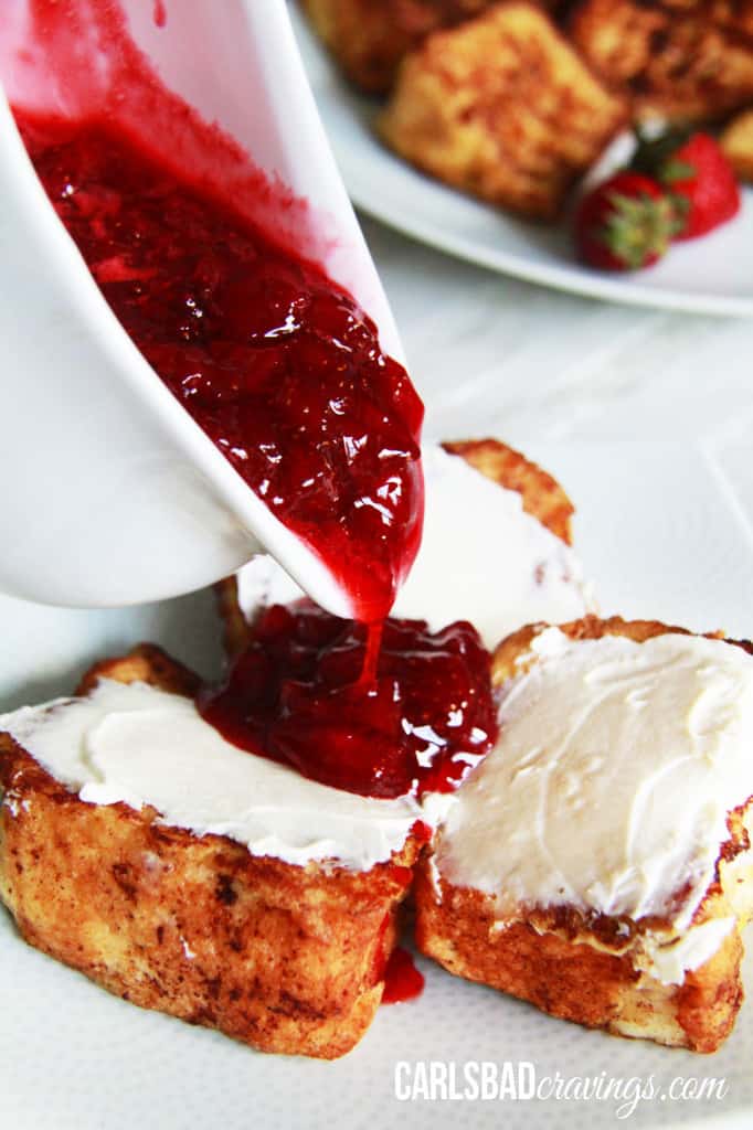 Home made Strawberry Syrup being poured out of a white bowl over three pieces of french toast. 