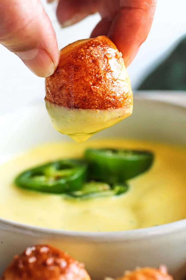 a hand pulling pretzel bites out of cheese sauce