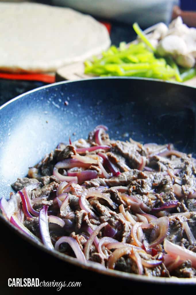 showing how to make  Philly Cheesesteak Pizza by cooking steek and onions