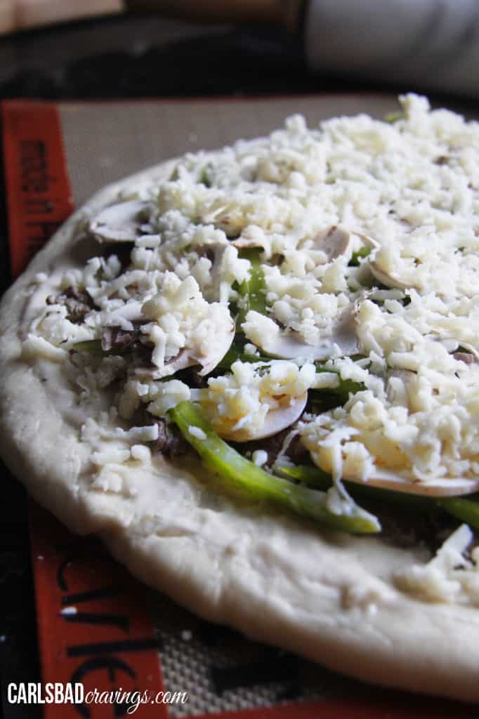 showing how to make  Philly Cheesesteak Pizza by layering pizza with mozzarella cheese