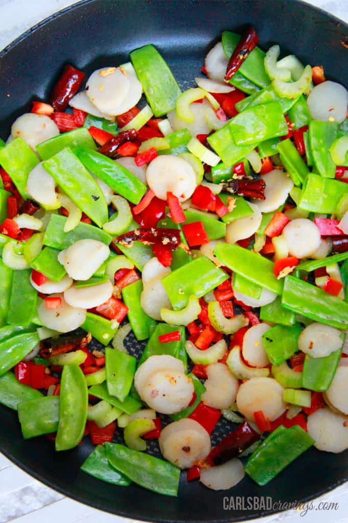 Showing how to make a Kung Pao Chicken Noodle Stir Fry by adding vegetables to the pan.