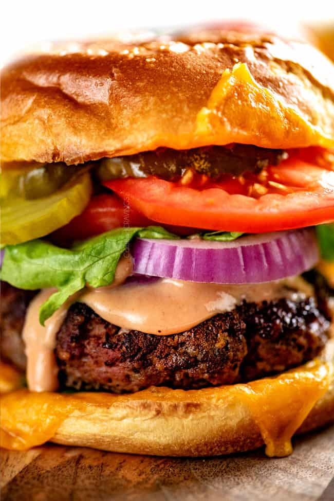 up close of homemade burger recipe topped with cheese, lettuce, tomatoes and onions