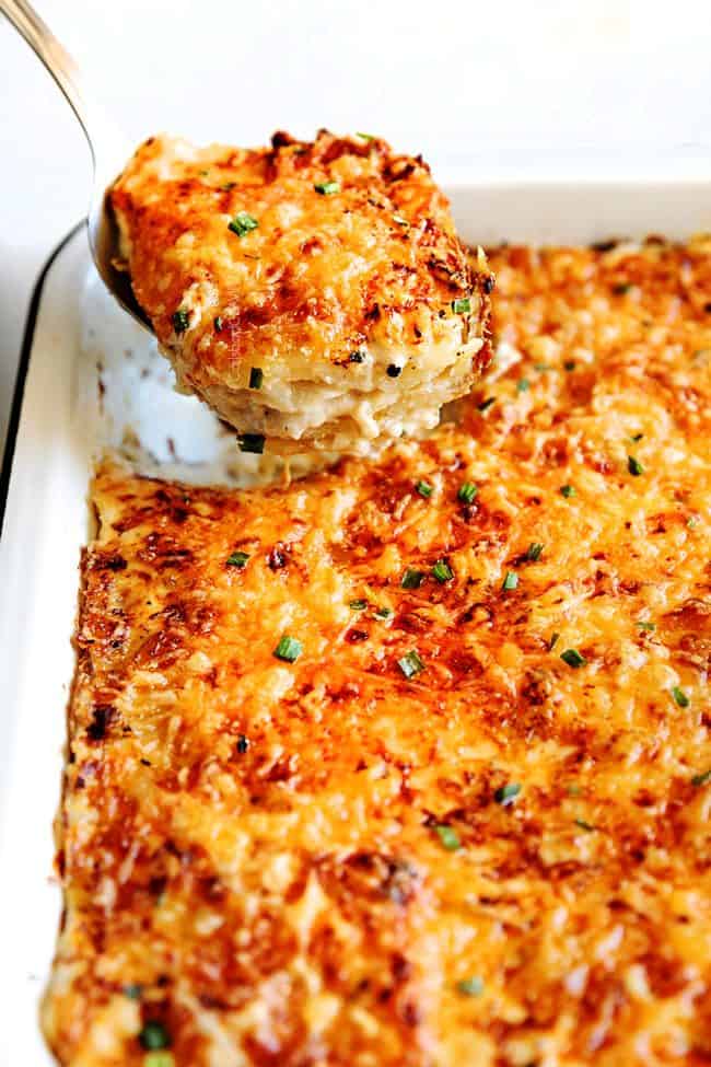 Au Gratin Potatoes with layers of potatoes, cheese and cream in a white casserole dish being scooped up
