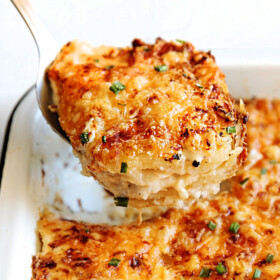 Potatoes Au Gratin with layers of potatoes, cheese and cream in a white casserole dish being scooped up