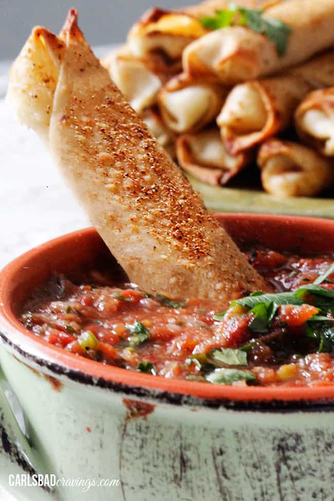 Close up image of a mozzarella stick in a bowl of salsa. 