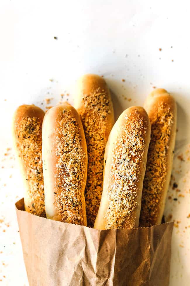 a bag of garlic parmesan breadsticks in a brown bag with parmesan and garlic herb seasoning laying on a white counter