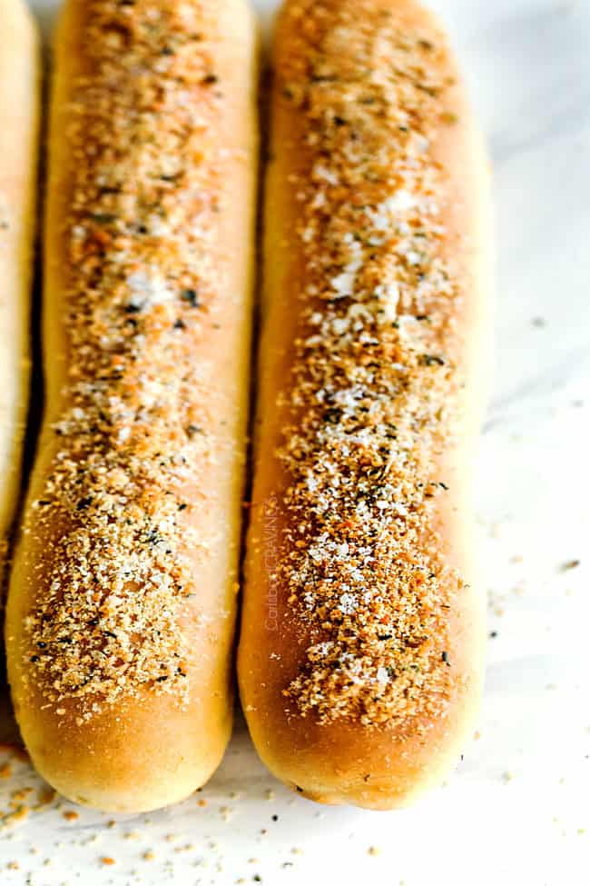 homemade breadsticks lined up in a row on a white marble counter