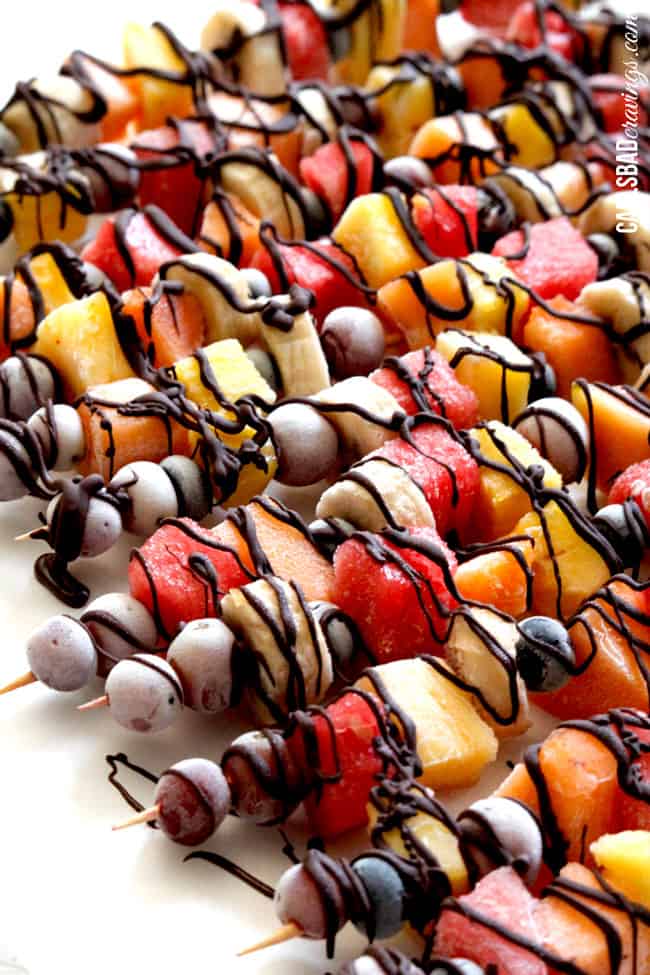 side view of rainbow fruit skewers on a white platter