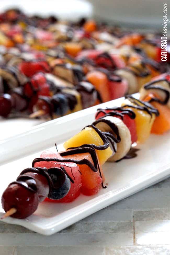 a fruit skewer with chocolate n a white serving plate