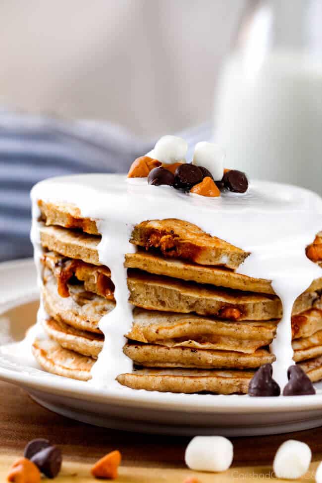 A tall stack of Fluffy S'mores Pancakes with marshmallow syrup over top. 