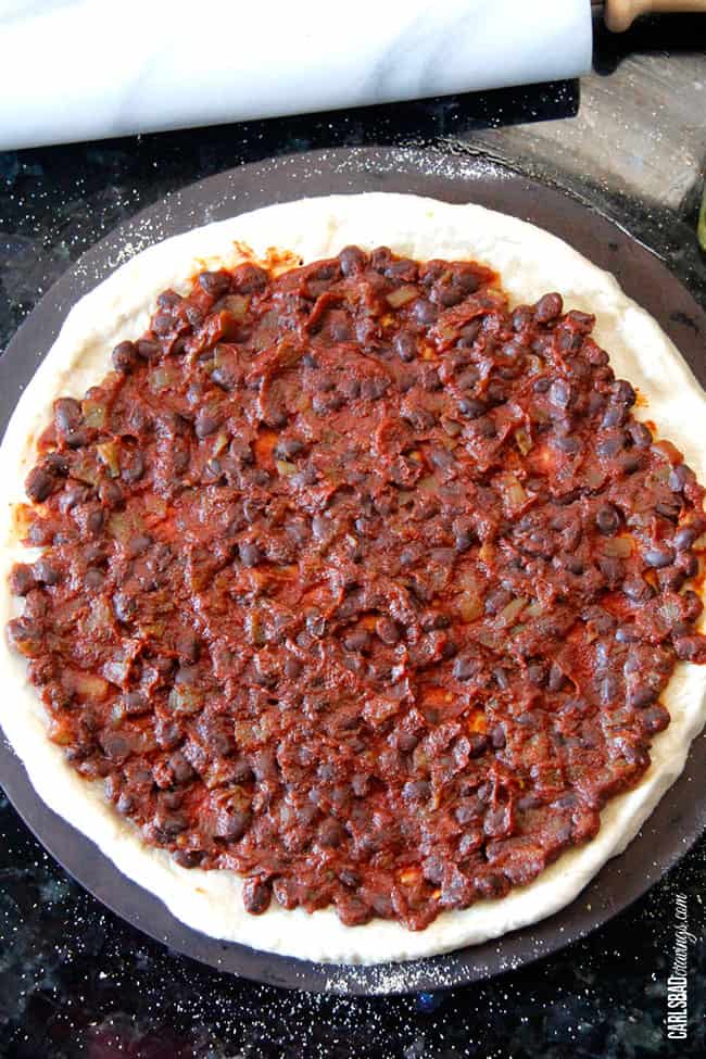 showing how to make pulled pork pizza by add tomato bean spread to pizza dough