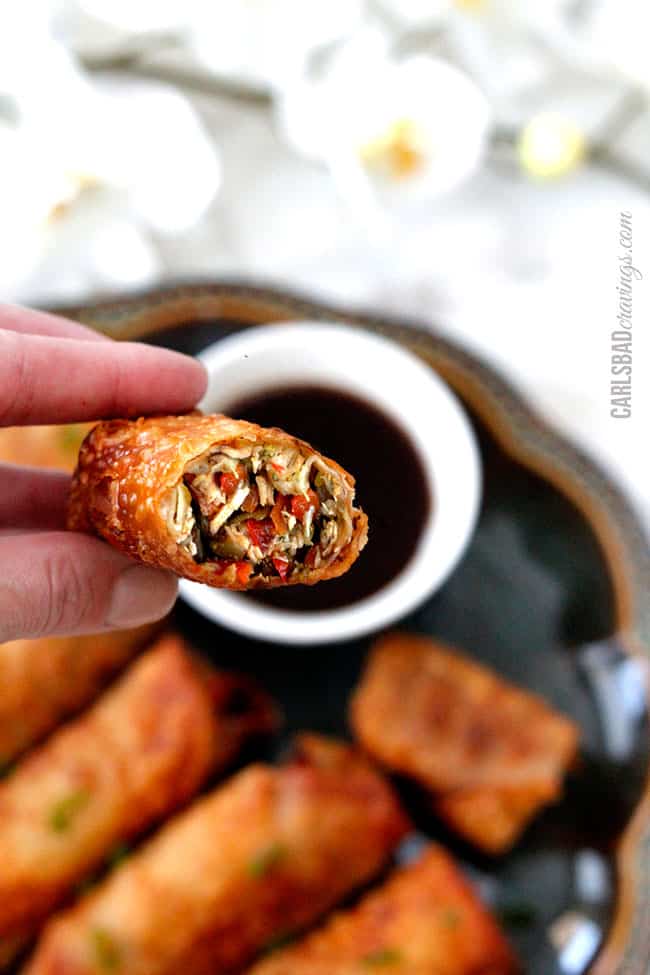 a hand holding a chicken egg roll that has been dunked in sweet and sour sauce