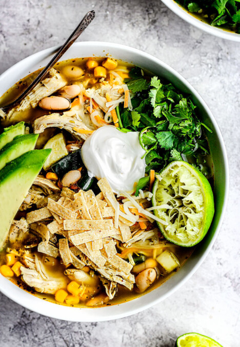 a bowl of easy crockpot chicken tortilla soup garnished with sour cream, avocados, cilantro and tortilla strips