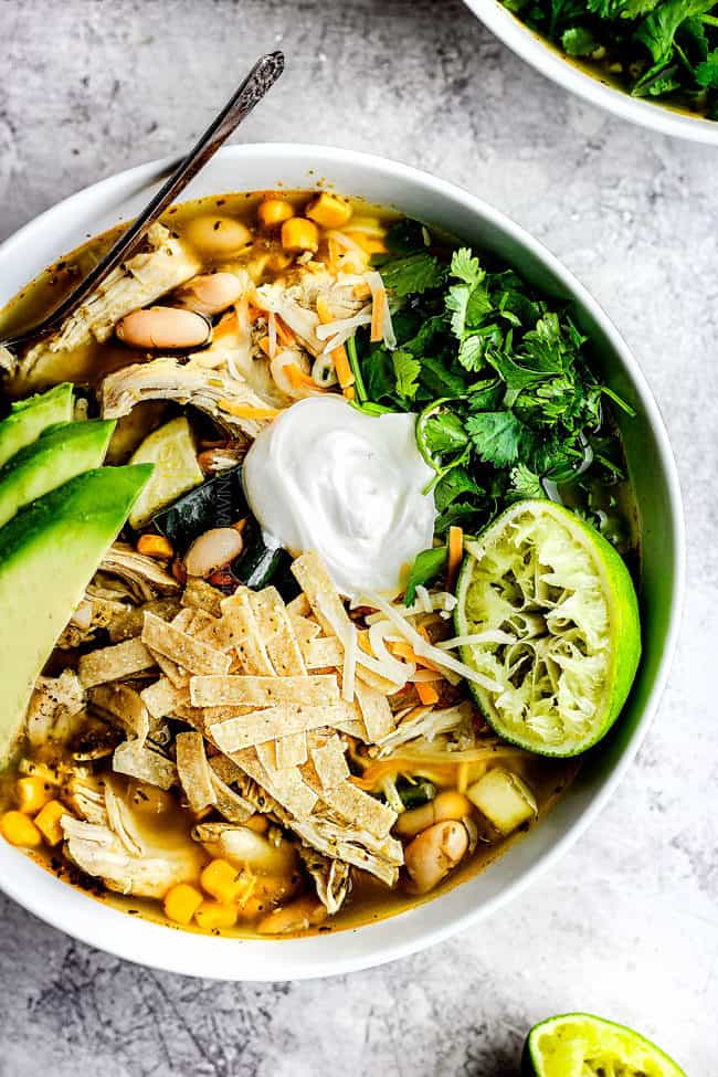 a bowl of easy crockpot chicken tortilla soup garnished with sour cream, avocados, cilantro and tortilla strips