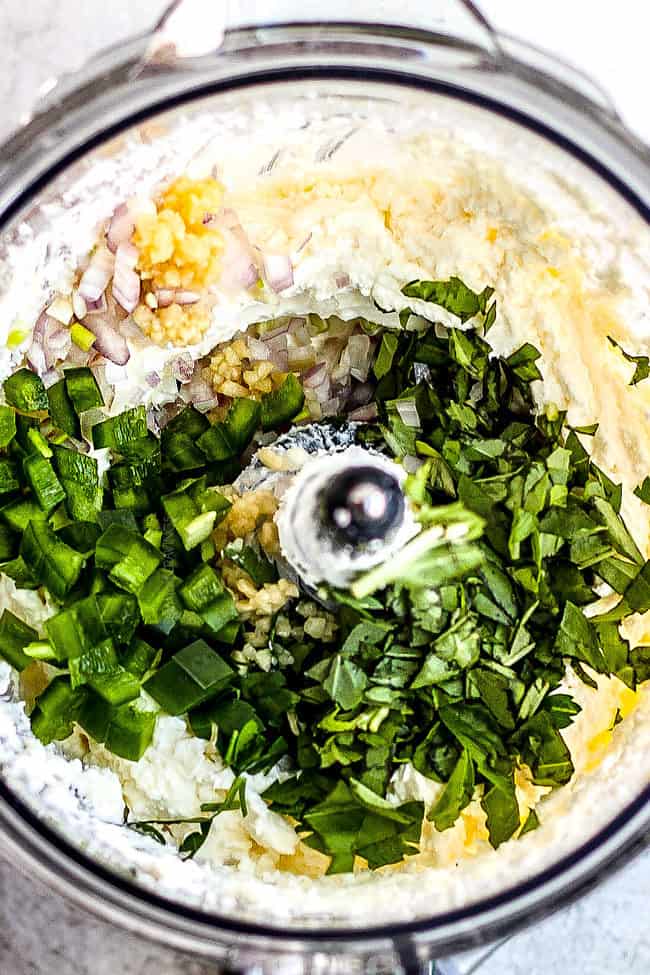 showing how to make feta dip by adding jalapenos, herbs, lemon juice to food processor