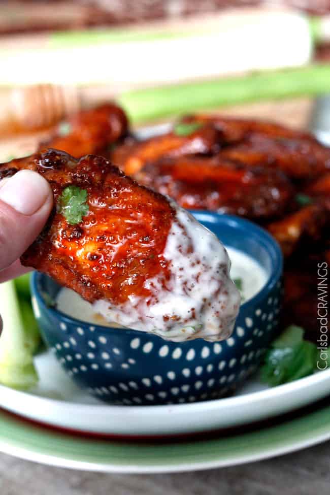 Close up showing the Honey Buffalo Hot Wings on a plate with celery and dipping a wing into the blue cheese dipping sauce. 
