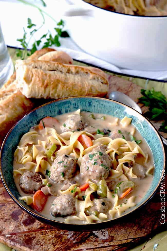 side view of a bowl of meatball soup with juicy meatballs, pasta, carrots, celery, mushrooms