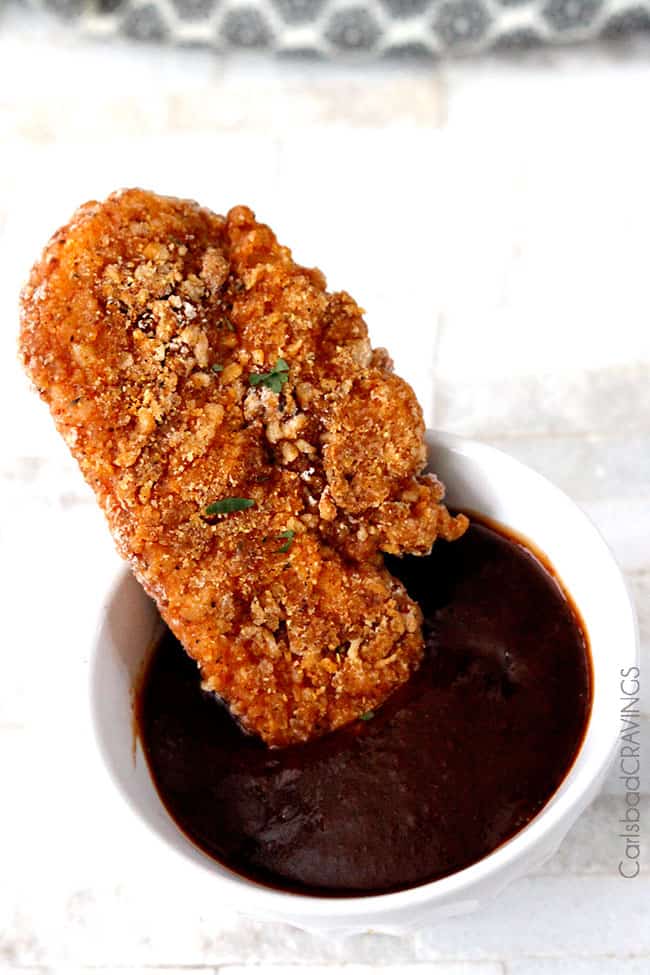 crispy oven fried chicken being dipped in barbecue sauce in a white bowl