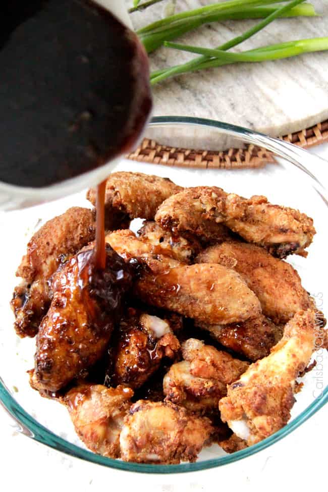 showing how to make chicken wings by pouring sauce over baked wings