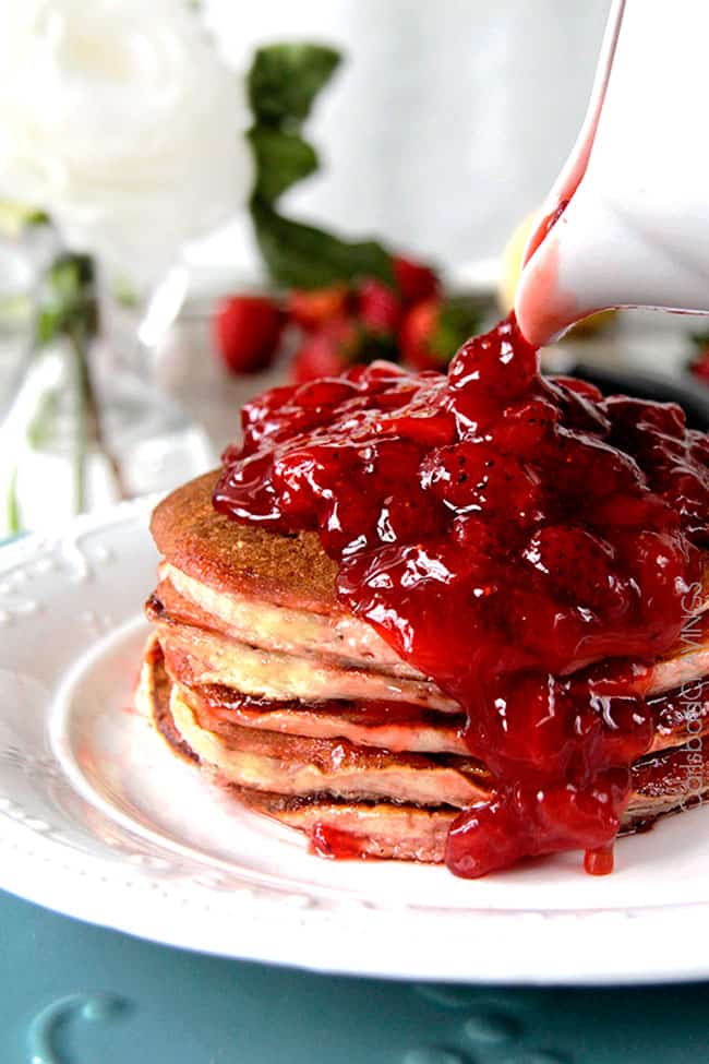 strawberry pancake syrup being poured over a stack of pancakes. 