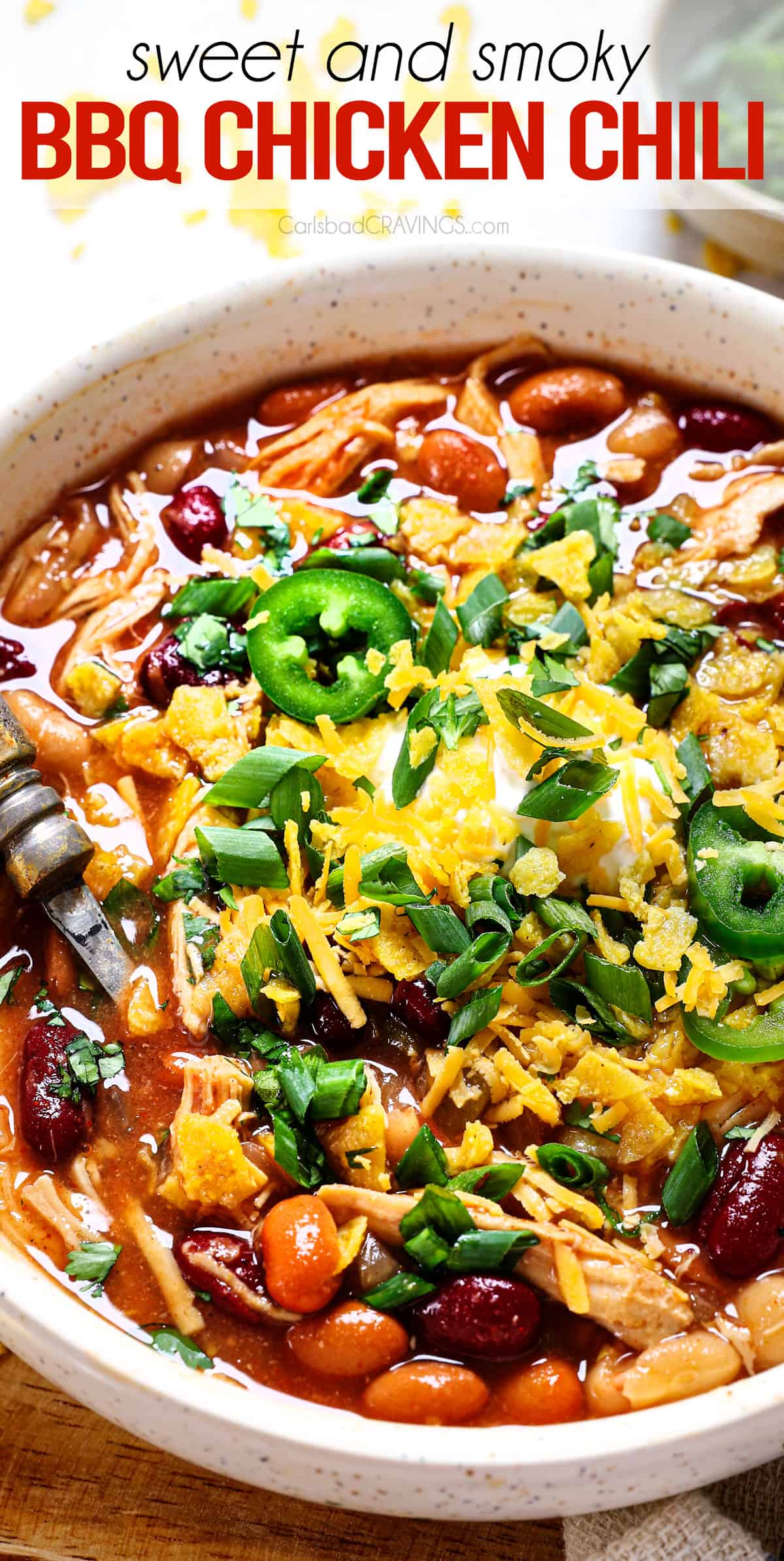 slow cooker chicken chili being served in a bowl with sour cream, tortilla chips, green onions and cheese