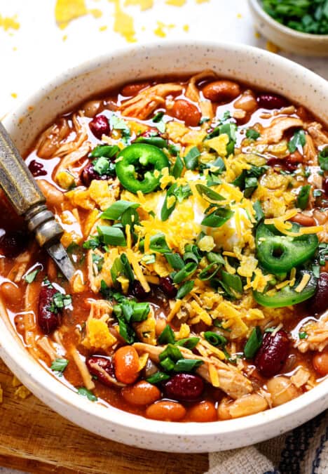 showing how to serve chicken chili by adding cheese, sour cream, green onions and tortilla chips