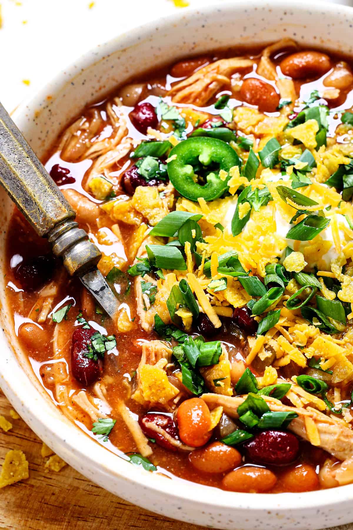 showing how to serve chicken chili by adding cheese, sour cream, green onions and tortilla chips