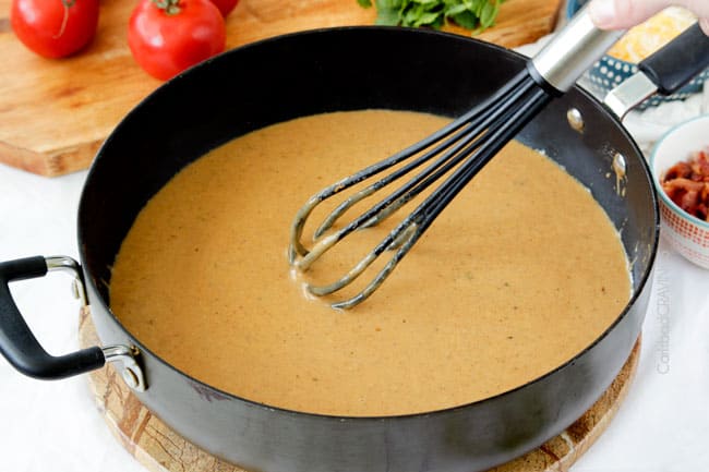 Showing how to make BBQ Ranch Chicken Pasta by mixing the cheese sauce in a black pan.