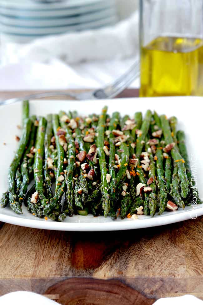 Front view of Fresh baked Roasted Asparagus on a white plate topped with nuts.