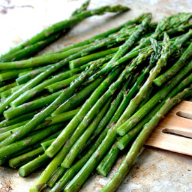 roasted asparagus on baking sheet being scooped up with a spatula