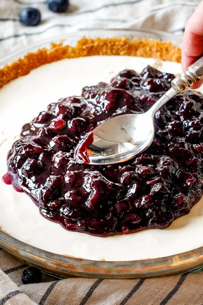 smoothing fresh blueberry sauce over cheesecake with the back of a spoon