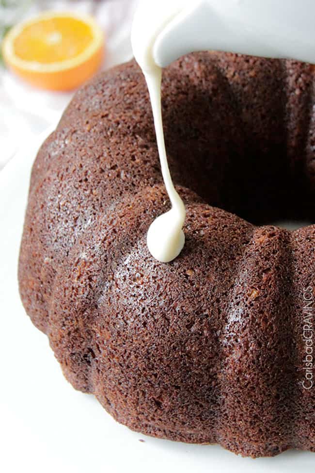 A full Carrot bundt Cake with Orange Glaze and orange zest pouring the icing drizzling down.