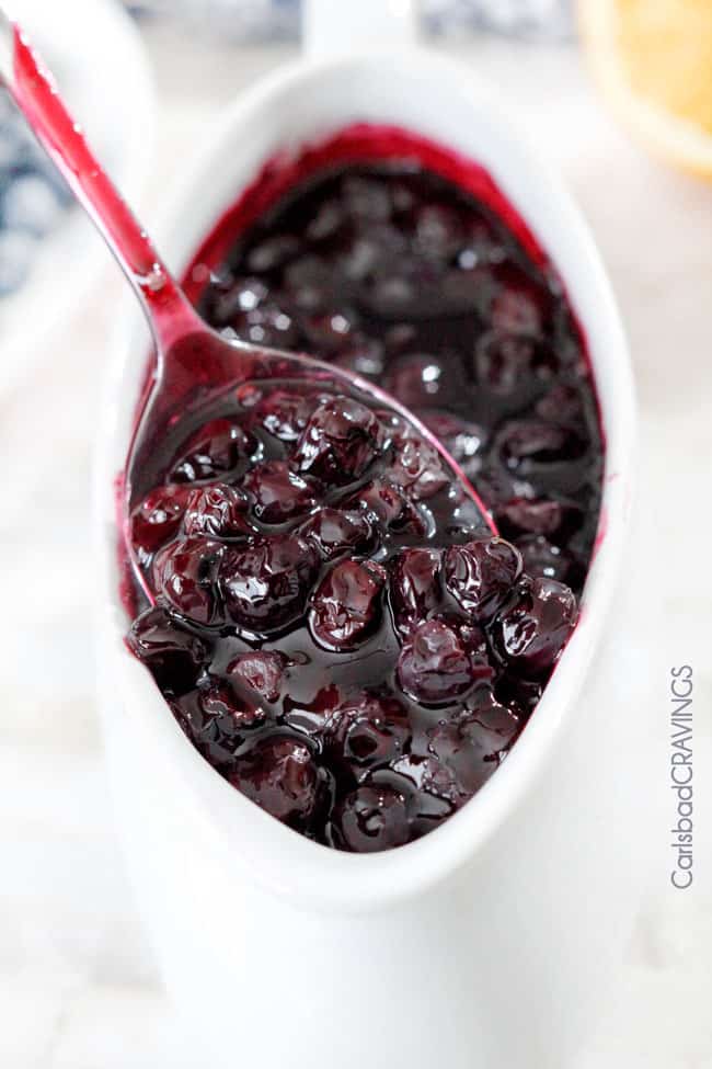 spooning fresh blueberry sauce from a white serving dish