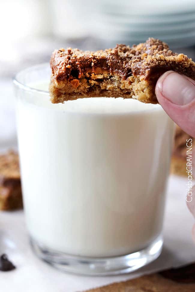 Close up view of Single Peanut Butter Cookie Bars held up in a hand next to a cup of milk.