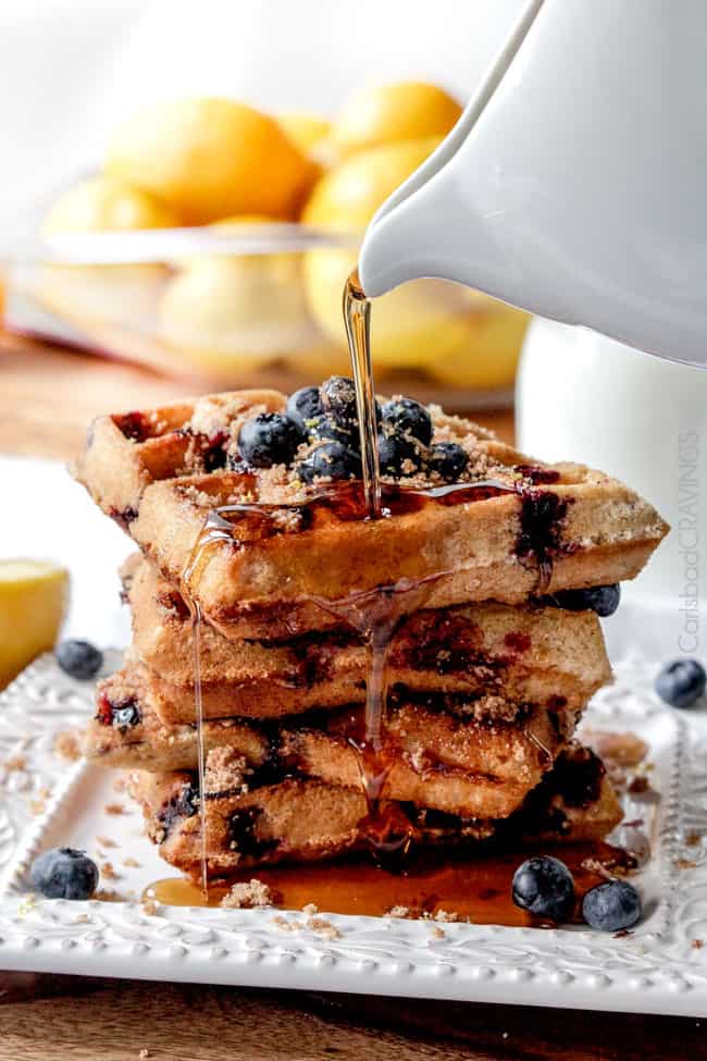 Close up view of a stack of four Blueberry Waffles on a white plate with blue berries. 