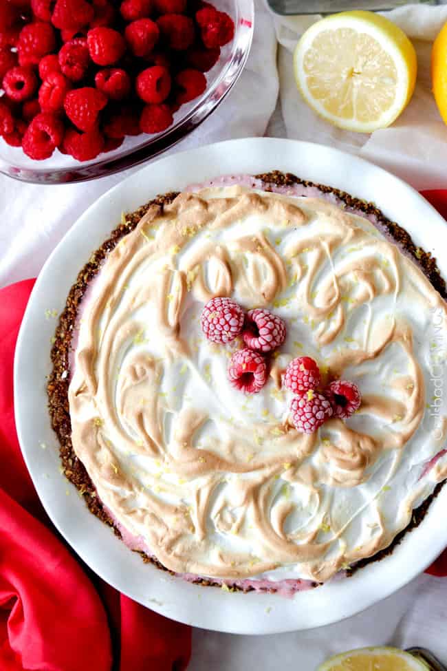 A full Frozen Lemon Meringue Pie top view on a white plate with raspberries and a fork. 