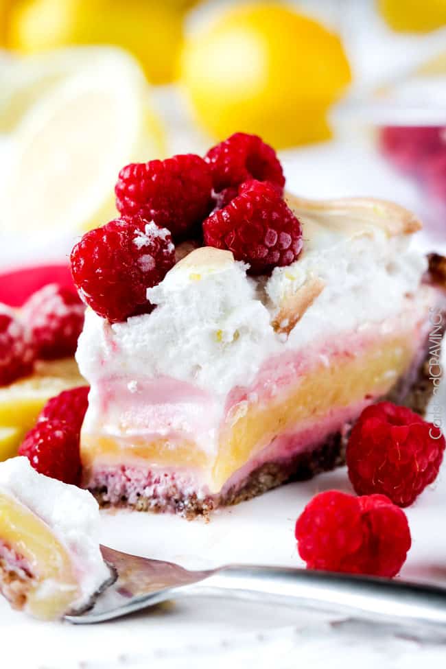 A close up view of Frozen Lemon Meringue Pie on a white plate with raspberries and a fork with a bite missing and a serving on a fork.. 