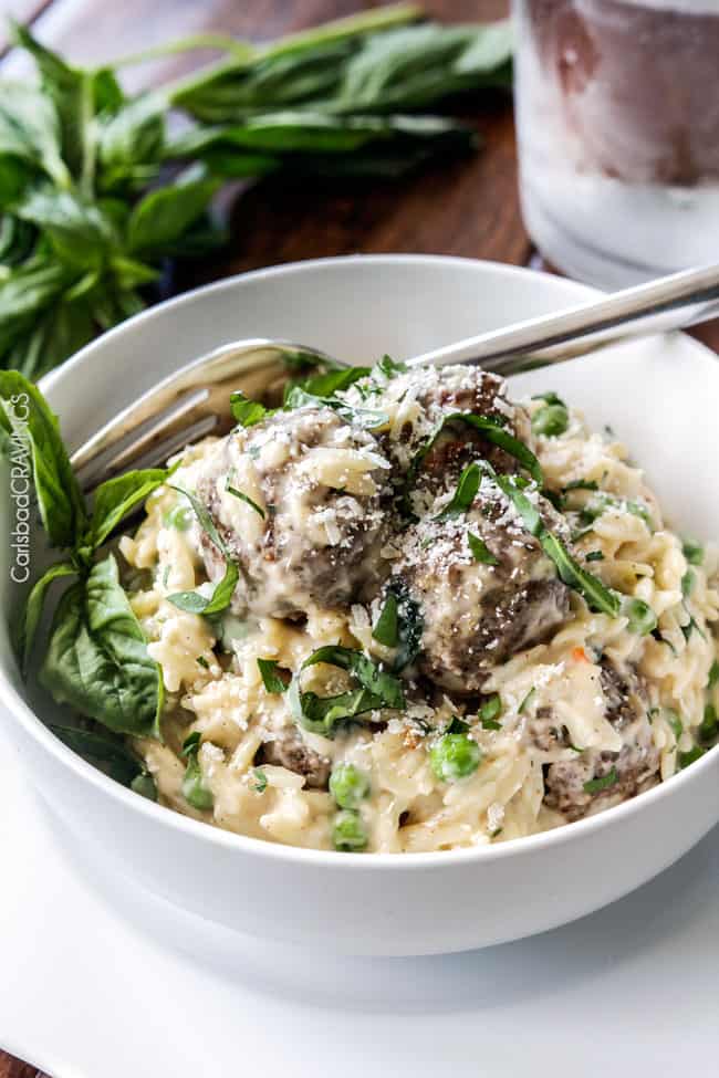 Parmesan Meatballs in a cream sauce with orzo and basil being served in a white bowl with a fork.