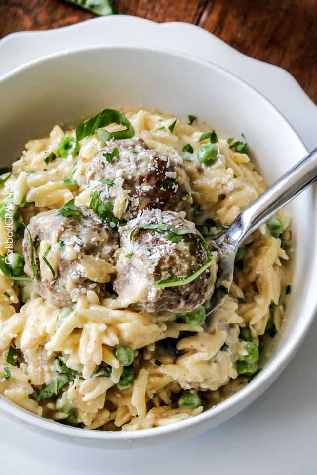 Top view of Parmesan Meatballs in a cream sauce with orzo and basil being served in a white bowl.