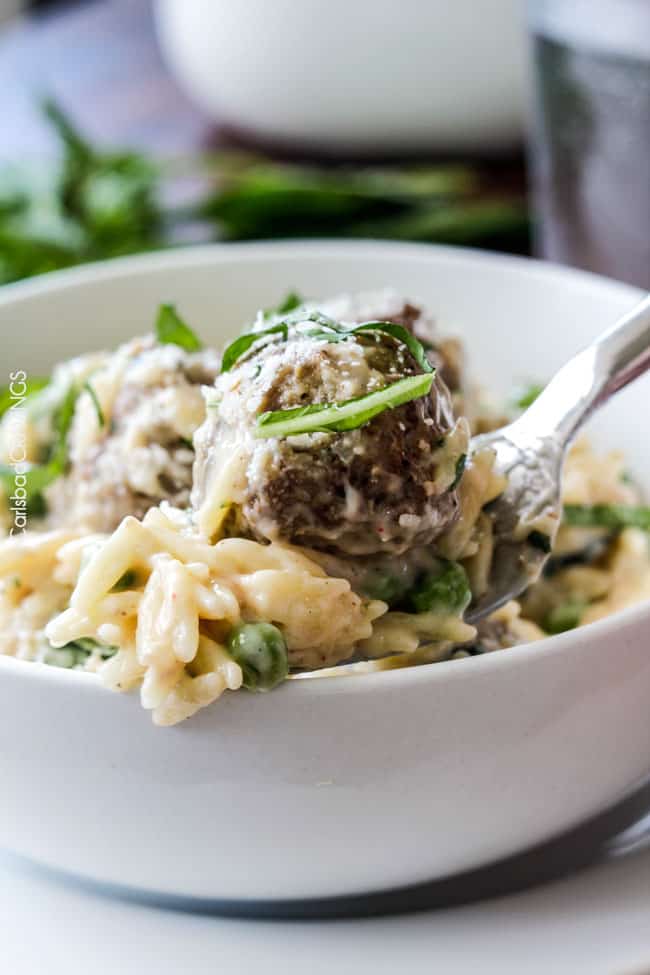 Close up of Parmesan Meatballs in a cream sauce with orzo and basil with a meatball on a fork. 