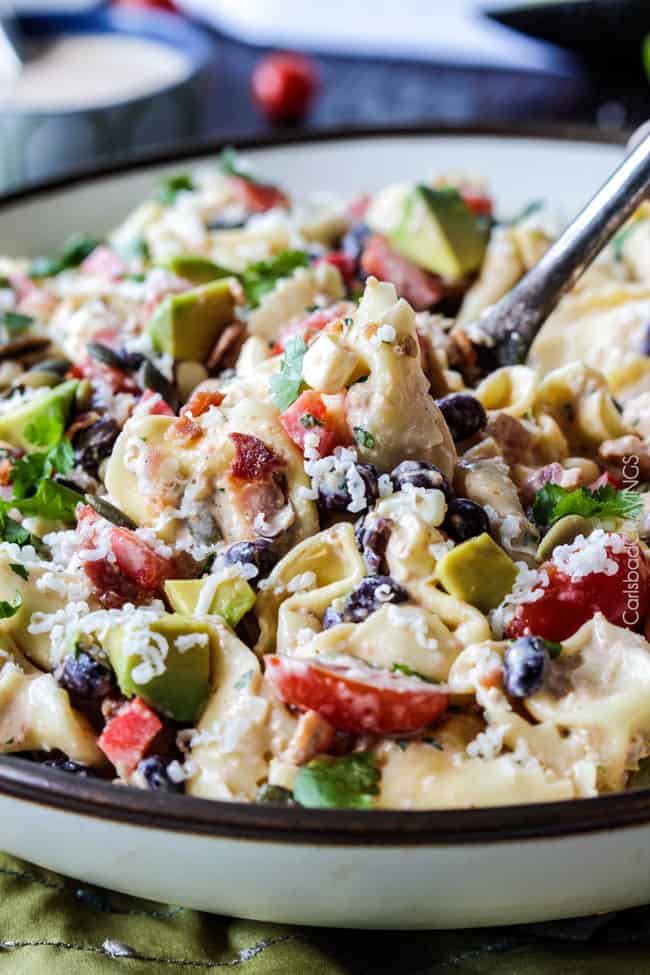 Make ahead, favorite potluck Southwest Pepper Jack Tortellini Salad = cheesy pillows of tortellini, sweet corn, black beans, avocado, bell peppers, etc. bathed in Creamy Salsa Dressing and garnished with bacon, Pepper Jack, sunflower seeds. Oh my YUM! #tortellini #pastasalad #southwest #salad