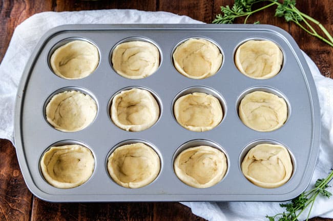 Showing how to make  Mini Deep Dish Hawaiian Pizzas by putting dough in a cup cake tin pan. .
