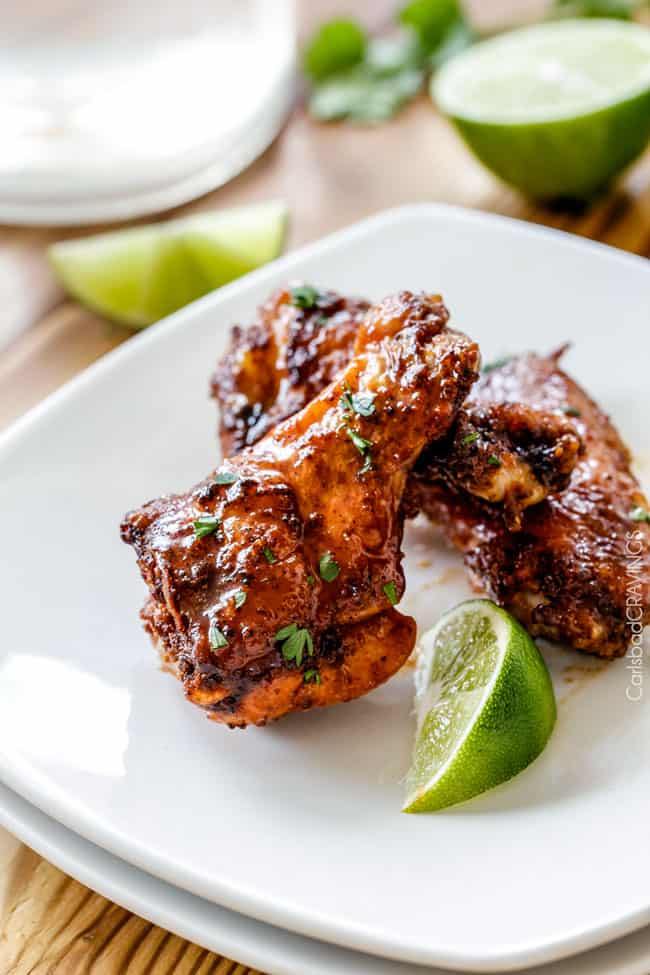 Side view of Baked Chipotle Honey Lime Hot Wings on a white plate with lime.